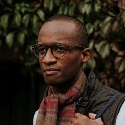 Image of Samuel Green. Short-cropped hair, black-rimmed glasses and a tartan scarf.